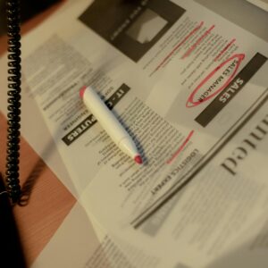 Close-up of a newspaper job section with a red marker and corded phone on a table.