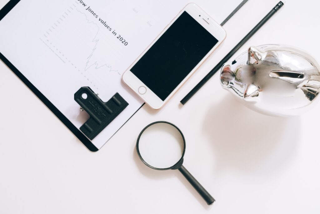 A flat lay of financial documents with a smartphone, magnifying glass, and piggy bank.