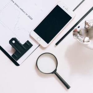 A flat lay of financial documents with a smartphone, magnifying glass, and piggy bank.